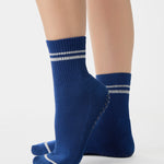 Women wearing a navy blue ankle grip sock with white stripes on the toes and top ankle cuff made for Pilates, Barre, Yoga, and beyond. 