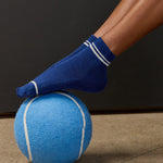 Women wearing a navy blue ankle grip sock with white stripes on the toes and top ankle cuff made for Pilates, Barre, Yoga, and beyond. 