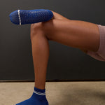 Women wearing a navy blue ankle grip sock with white stripes on the toes and top ankle cuff made for Pilates, Barre, Yoga, and beyond. 