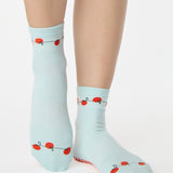 Woman wearing a solid light blue ankle grip sock with red tomatos on garden vines. Made for pilates, yoga, barre, and beyond. 