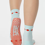 Woman wearing a solid light blue ankle grip sock with red tomatos on garden vines. Made for pilates, yoga, barre, and beyond. 