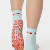 Woman wearing a solid light blue ankle grip sock with red tomatos on garden vines. Made for pilates, yoga, barre, and beyond. 