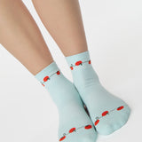Woman wearing a solid light blue ankle grip sock with red tomatos on garden vines. Made for pilates, yoga, barre, and beyond. 