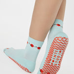 Woman wearing a solid light blue ankle grip sock with red tomatos on garden vines. Made for pilates, yoga, barre, and beyond. 
