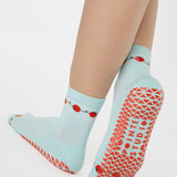 Woman wearing a solid light blue ankle grip sock with red tomatos on garden vines. Made for pilates, yoga, barre, and beyond. 
