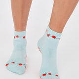 Woman wearing a solid light blue ankle grip sock with red tomatos on garden vines. Made for pilates, yoga, barre, and beyond. 