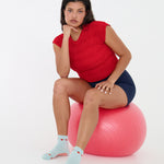 Woman wearing a solid light blue ankle grip sock with red tomatos on garden vines. Made for pilates, yoga, barre, and beyond. 
