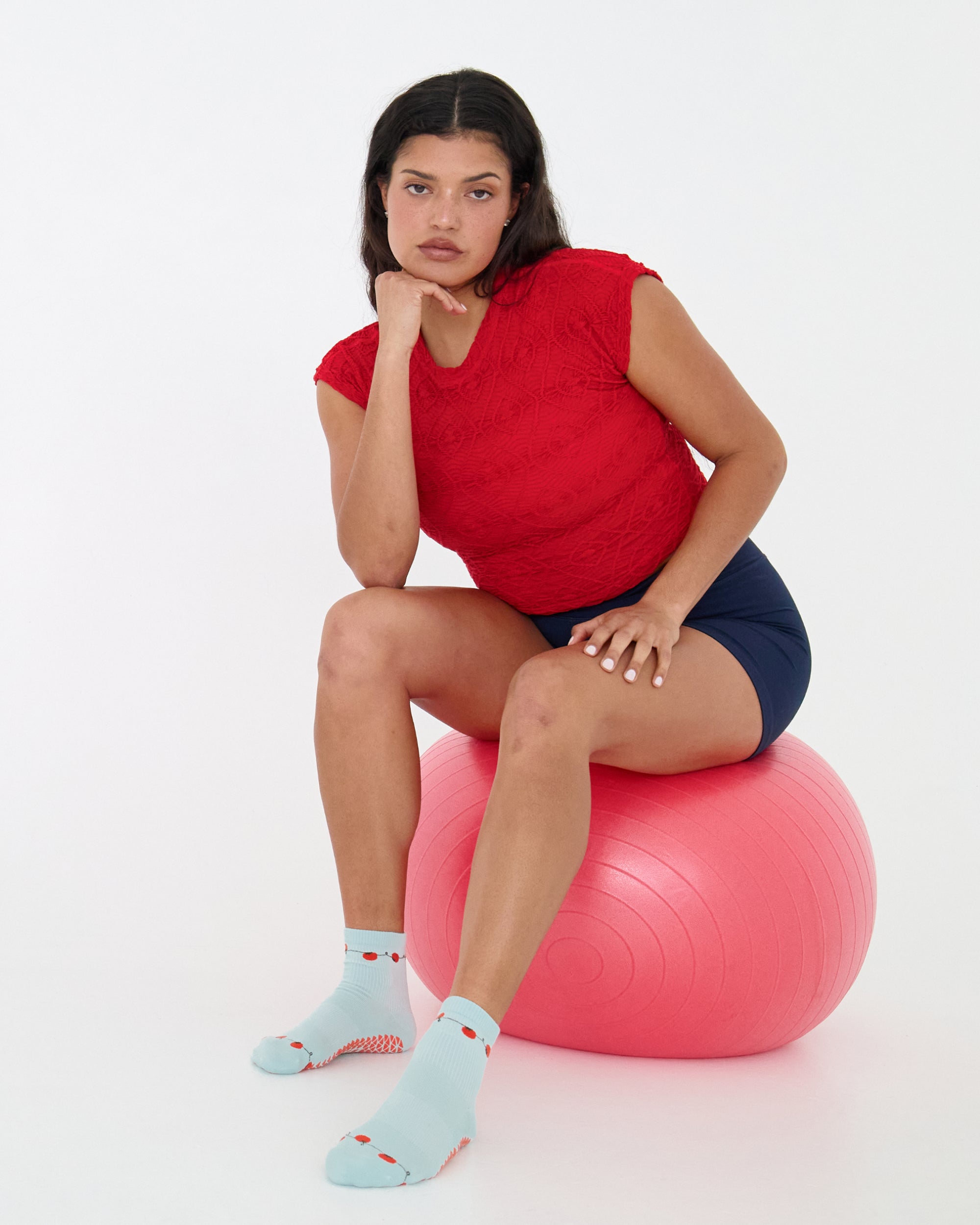 Woman wearing a solid light blue ankle grip sock with red tomatos on garden vines. Made for pilates, yoga, barre, and beyond. 