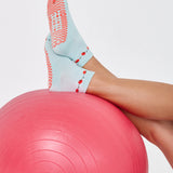 Woman wearing a solid light blue ankle grip sock with red tomatos on garden vines. Made for pilates, yoga, barre, and beyond. 