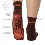 Woman wearing a solid chocolate brown ankle grip sock with orange stripes on the toes and top ankle cuff made for Pilates, Barre, Yoga, and beyond. With all product features.