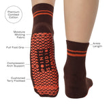 Woman wearing a solid chocolate brown ankle grip sock with orange stripes on the toes and top ankle cuff made for Pilates, Barre, Yoga, and beyond. With all product features.