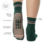 Woman wearing a solid green ankle grip sock with pink stripes on the toes and top ankle cuff made for Pilates, Barre, Yoga, and beyond. With product features listed.