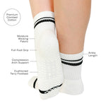 Women wearing a white ankle grip sock with black stripes on the toes and top ankle cuff made for Pilates, Barre, Yoga, and beyond with a list of product features.