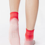 Woman wearing a pink ombre ankle grip sock, made for pilates, barre, yoga, and beyond.