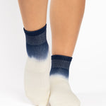 Woman wearing a blue to white ombre ankle grip sock, made for pilates, barre, yoga, and beyond.