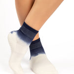 Woman wearing a blue to white ombre ankle grip sock, made for pilates, barre, yoga, and beyond.
