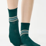 Women wearing a dark green ankle grip sock with 3 stripes on the ankle made for Pilates, Barre, Yoga, and beyond. 