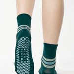 Women wearing a dark green ankle grip sock with 3 stripes on the ankle made for Pilates, Barre, Yoga, and beyond. 