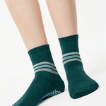 Women wearing a dark green ankle grip sock with 3 stripes on the ankle made for Pilates, Barre, Yoga, and beyond. 