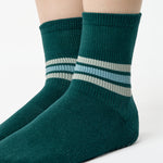 Women wearing a dark green ankle grip sock with 3 stripes on the ankle made for Pilates, Barre, Yoga, and beyond. 