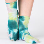 Woman wearing a tie dye green and blue ankle grip sock, made for pilates, barre, yoga, and beyond.  