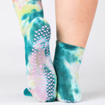 Woman wearing a tie dye green and blue ankle grip sock, made for pilates, barre, yoga, and beyond.  