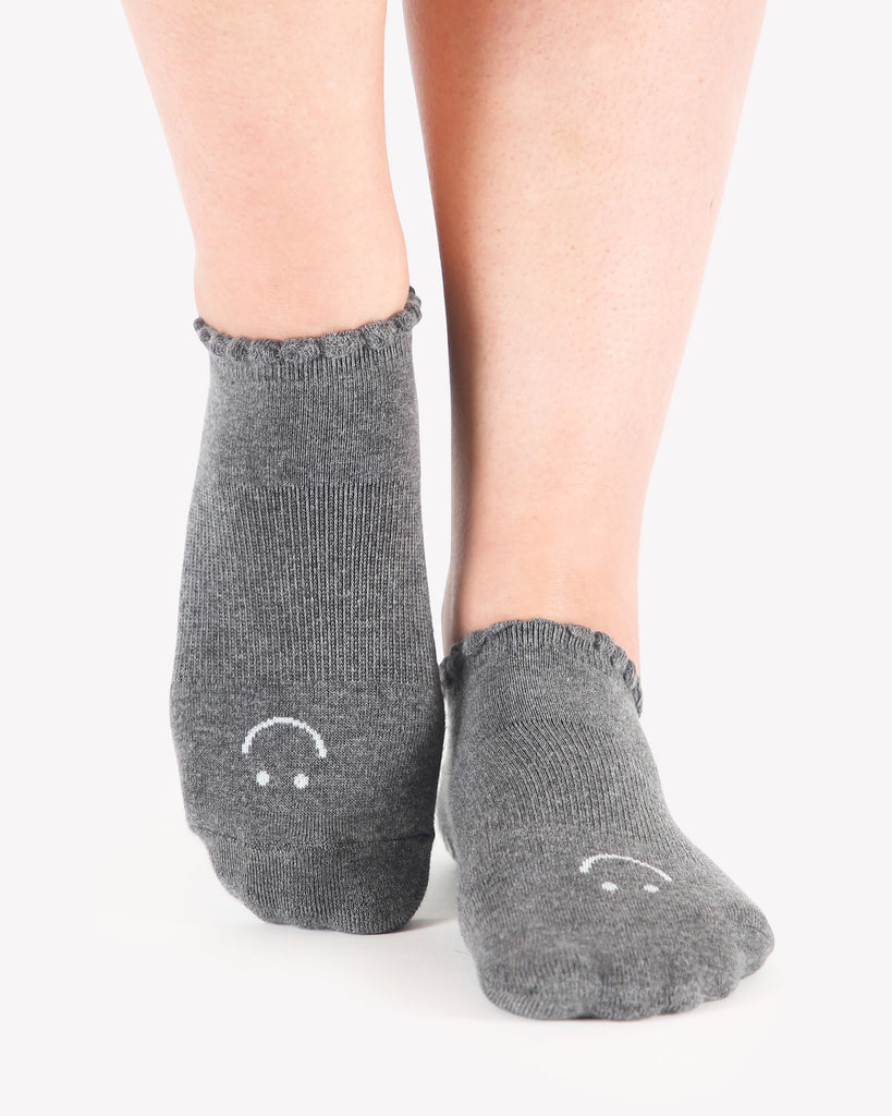 Close up photo of a woman's feet wearing grey socks with a happy face on the top of the foot
