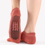 Woman wearing a rusty red aragon strap grip sock, made for pilates, barre, yoga, and beyond. 