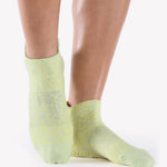 Woman wearing a light lime green full foot grip sock with green squiggly lines, made for pilates, barre, yoga, and beyond.  