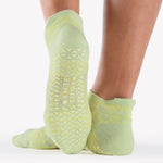 Woman wearing a light lime green full foot grip sock with green squiggly lines, made for pilates, barre, yoga, and beyond.  