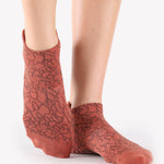 Woman wearing a terracotta rusty red full foot grip sock with dark brown squiggly lines, made for pilates, barre, yoga, and beyond.  