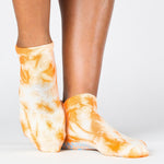 Woman wearing a bright orange full foot grip sock with it tie dyed white, made for pilates, barre, yoga, and beyond.  