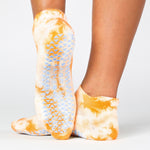 Woman wearing a bright orange full foot grip sock with it tie dyed white, made for pilates, barre, yoga, and beyond.  