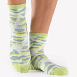 Woman wearing a light green ankle grip sock with green animal print, made for pilates, barre, yoga, and beyond.  