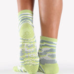 Woman wearing a light green ankle grip sock with green animal print, made for pilates, barre, yoga, and beyond.  