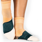 Woman wearing an orange ankle grip sock with a solid green stripe in the center, made for pilates, barre, yoga, and beyond.  