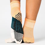Woman wearing an orange ankle grip sock with a solid green stripe in the center, made for pilates, barre, yoga, and beyond.  