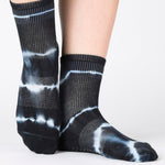 Woman wearing a black ankle grip sock with white curved lines, made for pilates, barre, yoga, and beyond.  