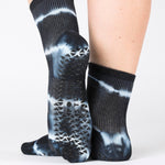 Woman wearing a black ankle grip sock with white curved lines, made for pilates, barre, yoga, and beyond.  