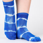 Woman wearing a bright blue ankle grip sock with white curved lines, made for pilates, barre, yoga, and beyond.  