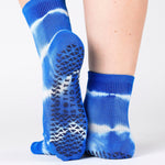 Woman wearing a bright blue ankle grip sock with white curved lines, made for pilates, barre, yoga, and beyond.  