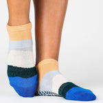 Woman wearing a bold striped grip sock with blue and orange toned stripes, made for pilates, barre, yoga, and beyond. 
