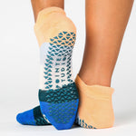 Woman wearing a bold striped grip sock with blue and orange toned stripes, made for pilates, barre, yoga, and beyond. 