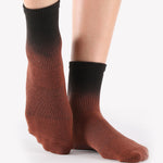 Woman wearing an ombre black to a brown terracotta red ankle grip sock, made for pilates, barre, yoga, and beyond.  