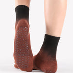 Woman wearing an ombre black to a brown terracotta red ankle grip sock, made for pilates, barre, yoga, and beyond.  