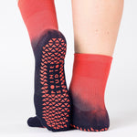Woman wearing a ombre red black grip sock, made for pilates, barre, yoga, and beyond.  