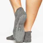 Woman wearing a solid charcoal grey strap grip sock, made for pilates, barre, yoga, and beyond. 